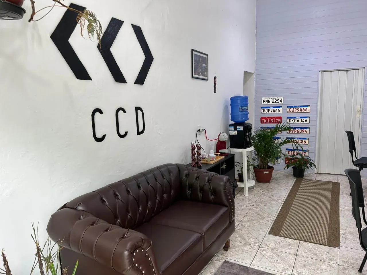 Recepção da CCD Despachante, com o símbolo da empresa na parede, sofá de espera e placas de veículos expostas